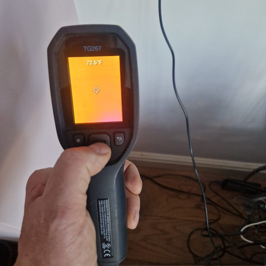 Thermal camera showing that the wall is not Damp Handheld thermal imaging camera displaying an orange heat map on the screen.